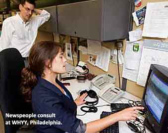Woman gestures at computer screen while consulting with colleague