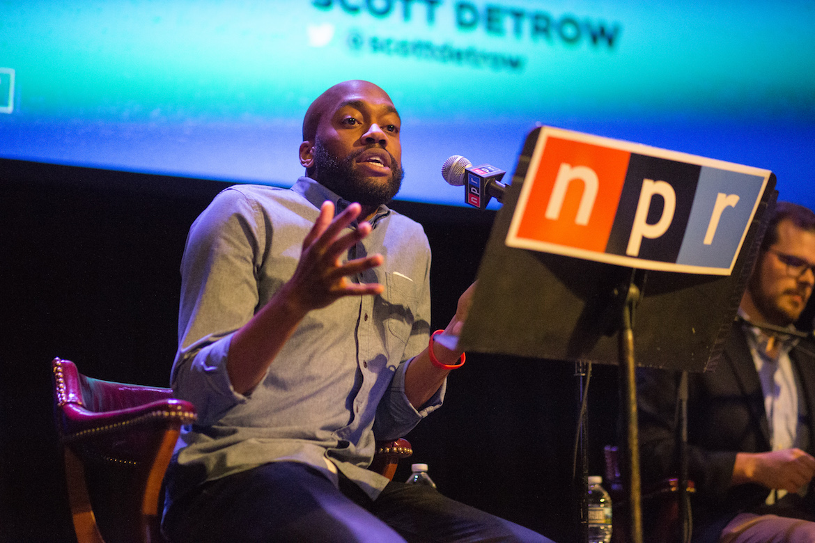 Sam Sanders speaks into a microphone during a live event.