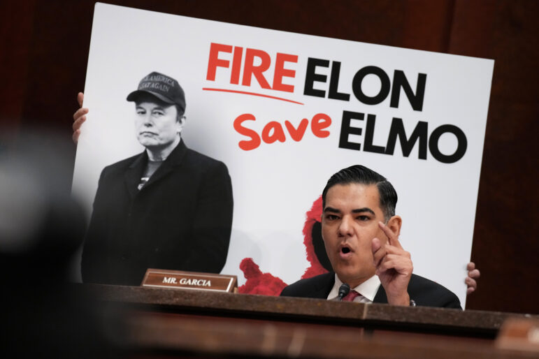 Rep. Robert Garcia (D-Calif.) speaks during the hearing in front of a poster that says "Fire Elon Save Elmo" and that depicts Elon Musk and Elmo from "Sesame Street."