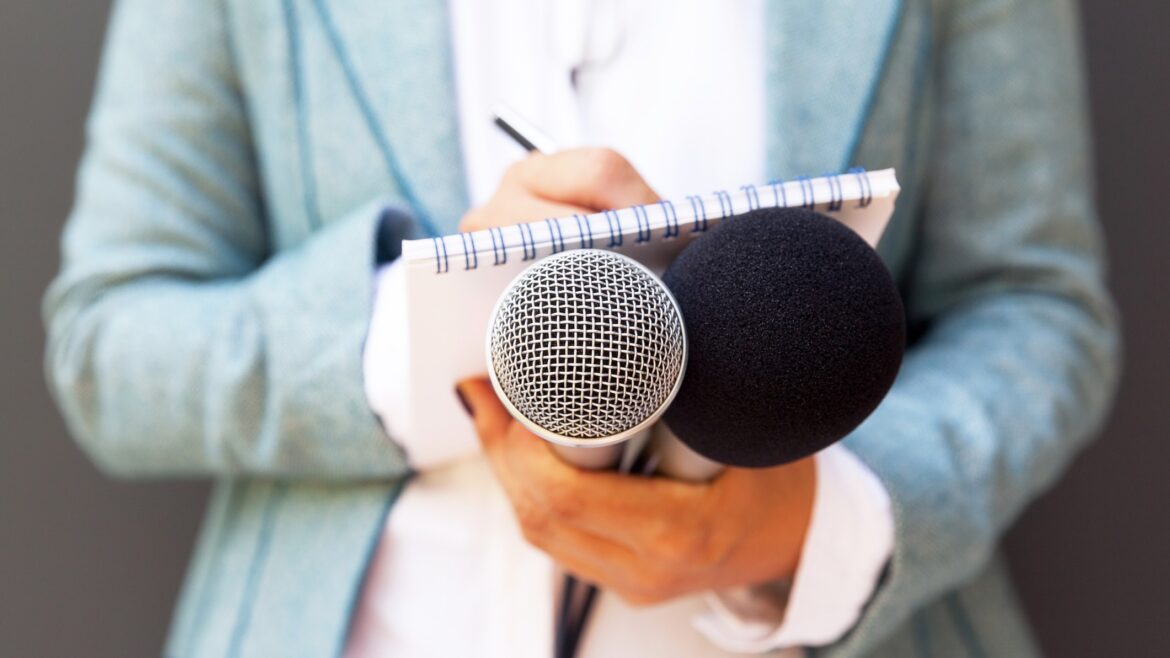 Female reporter at press conference, writing notes, holding microphone