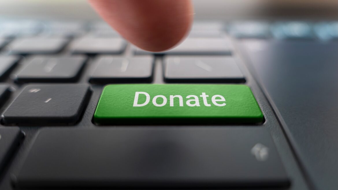 Finger pressing green "Donate" key on a laptop keyboard