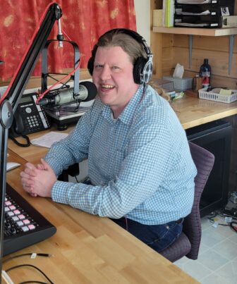 Man sitting in radio studio smiling with headphones on
