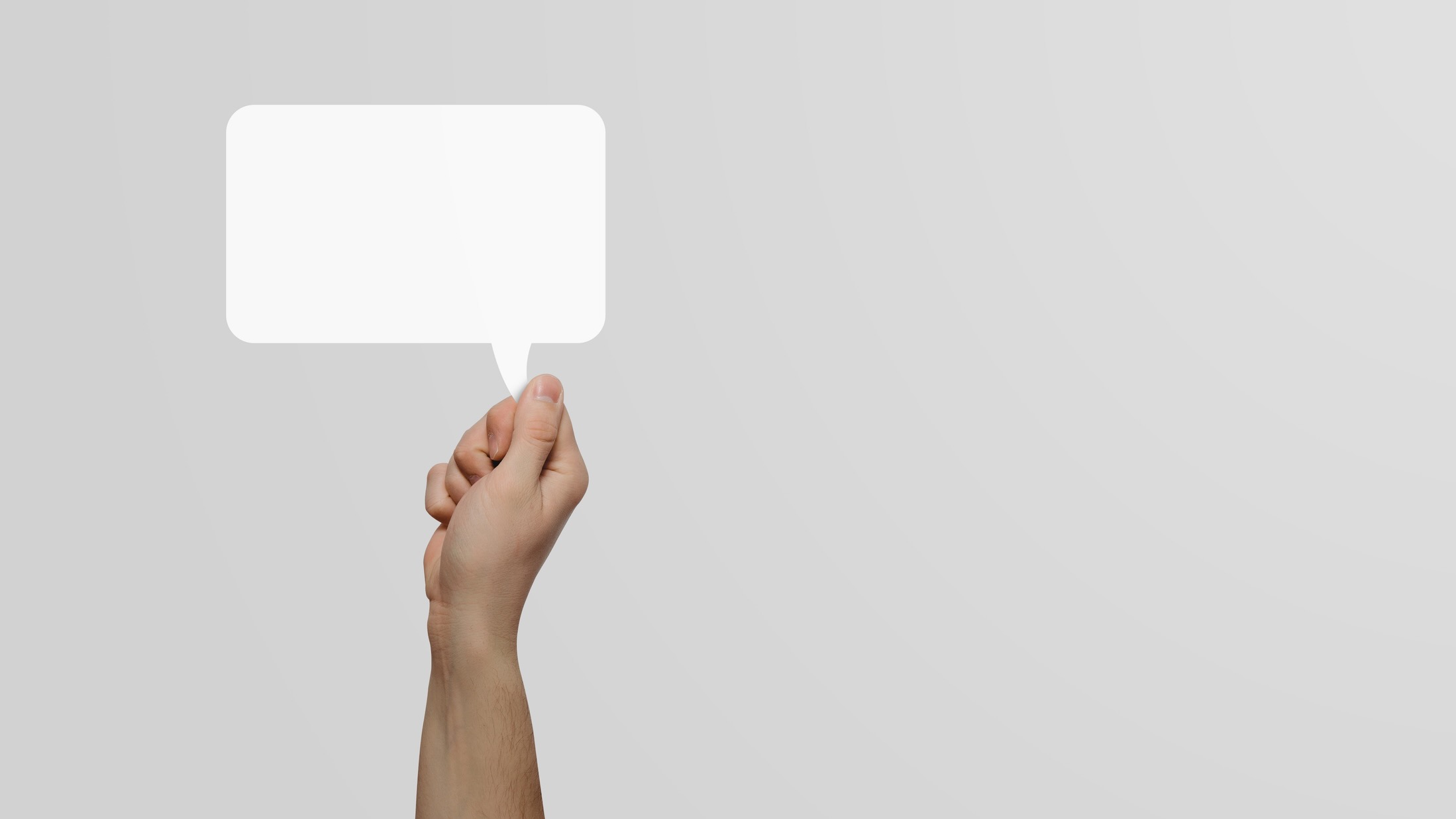 A hand holds an empty speech balloon against a monochrome background