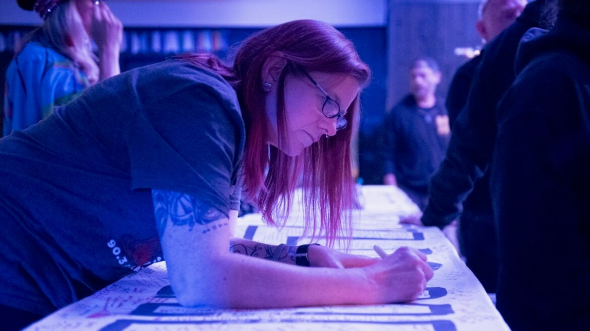 A listener signs a banner reading “I STAND WITH PUBLIC MEDIA” in KEXP's gathering space.