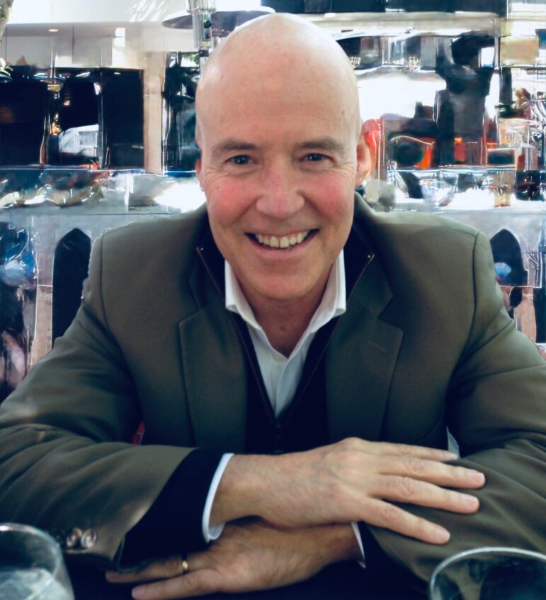 Steve Lama, seated with his arms folded and smiling