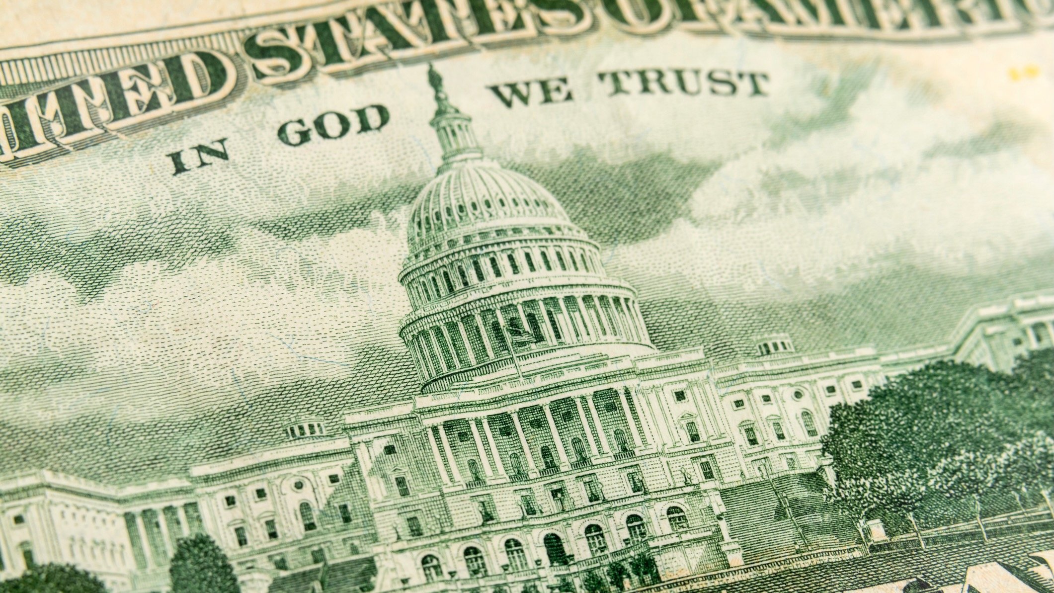 Close-up of the U.S. Capitol building as it appears on U.S. currency, showing detailed engraving with the words “In God We Trust” above.