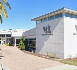 Exterior view of the WFIT 89.5 FM Broadcast Center, a modern low-rise building with large windows, surrounded by palm trees and landscaped greenery under a clear blue sky.