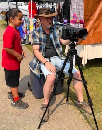 A child watches as Nebraska Public Media's Chad Davis set up a camera on the powwow grounds.