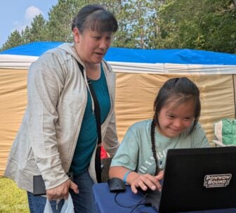 A mother watches her daughter play a demo of the game at this year's Menominee Contest Powwow.