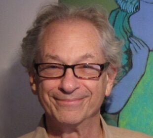 Headshot of Martin Perlich, an older man with gray hair and glasses, who is smiling warmly at the camera. He is wearing a beige shirt and standing in front of a colorful painting that includes a blue and green figure.