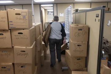 A volunteer walks between boxes in a KCUR storage room.
