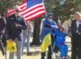 Wyoming Public Radio listener Richard Garrett speaks into a microphone at an outdoor rally while people stand nearby holding an American flag.