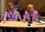 Nashville PBS CEO Becky Magura and PBS CEO Paula Kerger sit at a table during a public meeting. Kerger, wearing a pink blazer, speaks into a microphone while papers, a phone and a water bottle sit in front of her. Magura, in a purple sweater, sits beside her listening, while a man behind them looks down at a phone. Chairs and meeting-room equipment are visible in the background.