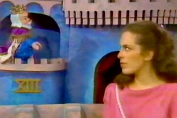 A scene from "Mister Rogers’ Neighborhood" shows Lady Aberlin in a pink top looking to the side, while King Friday XIII, a puppet wearing a crown, sits in a castle window.