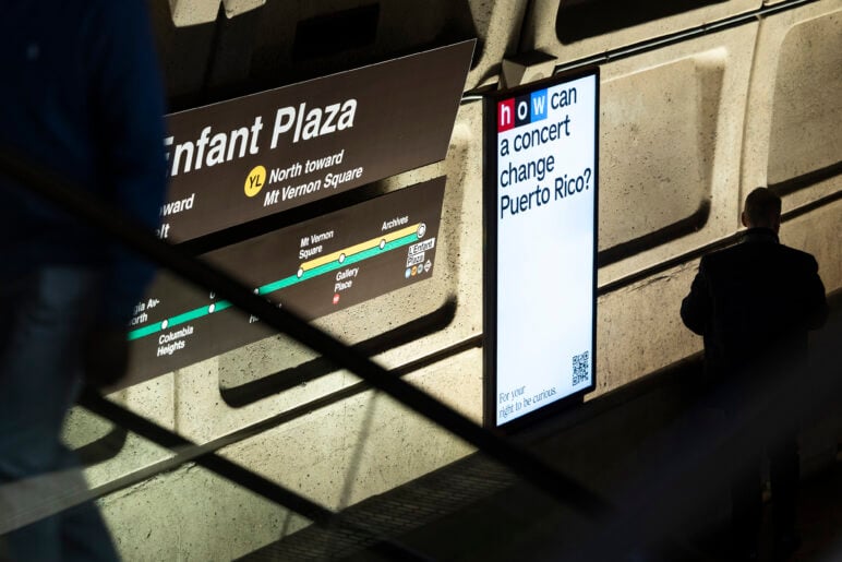 Digital display promoting NPR is mounted on a wall inside the L’Enfant Plaza Metro station in Washington, D.C. A commuter walks past in shadow while the screen asks, “How can a concert change Puerto Rico?”