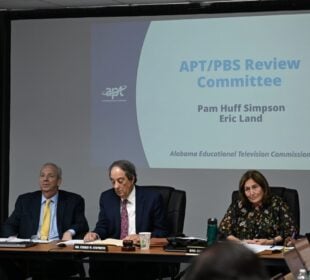 Members of the Alabama Educational Television Commission sit at a conference table during a meeting, with a projected slide behind them reading “APT/PBS Review Committee,” listing Pam Huff Simpson and Eric Land, Alabama Educational Television Commission.