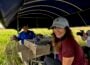 "LA64" host Karen LeBlanc smiles while sitting on a boat in a marsh as Barry Toups demonstrates crawfish harvesting equipment and Ryan Hamilton films the scene.