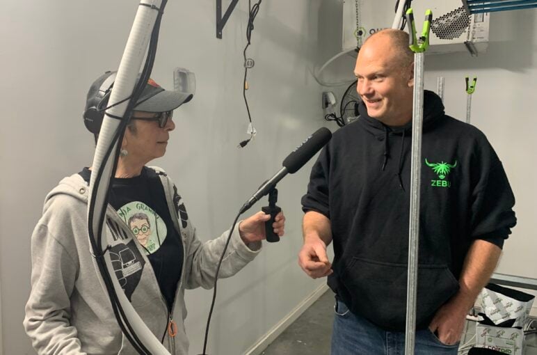 Karen Michel holds a microphone while interviewing a cultivator inside a cannabis cultivation facility.