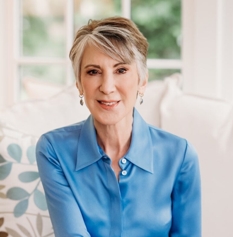 Headshot of Carly Fiorina, seated indoors and smiling at the camera while wearing a light blue blouse.