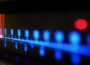 Close-up of an illuminated FM radio tuner dial, with blue frequency markings and a glowing orange indicator positioned near 92 on the scale. The image uses shallow focus, leaving much of the dial softly blurred against a dark background.
