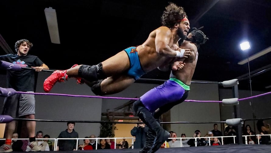 Tobias Storm launches horizontally into a flying tackle against "The Realist" Calvin Aldridge in a Show-Me State Wrestling match as spectators watch from ringside.