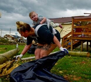 Kaitlyn Robinson picks up storm debris with her daughter, Olivia, strapped to her back in Laurel County, Ky., in May 2025