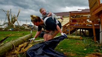Kaitlyn Robinson picks up storm debris with her daughter, Olivia, strapped to her back in Laurel County, Ky., in May 2025