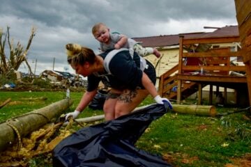Kaitlyn Robinson picks up storm debris with her daughter, Olivia, strapped to her back in Laurel County, Ky., in May 2025