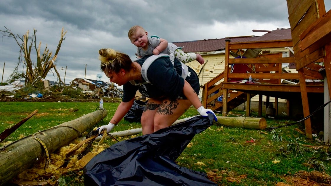 Kaitlyn Robinson picks up storm debris with her daughter, Olivia, strapped to her back in Laurel County, Ky., in May 2025