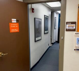 An open door leads into the KTEP-FM studios at the University of Texas at El Paso. A sign identifies the entrance as “206 KTEP FM Studios,” while campus flyers hang on a bulletin board outside the studio hallway.