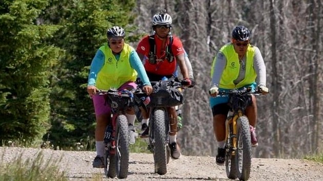 Three mountain bikers cycle along a gravel trail near the woods.
