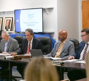Members of the Alabama Educational Television Commission sit at a conference table during a meeting as a screen displays “Executive Director Highlights.”