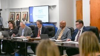 Members of the Alabama Educational Television Commission sit at a conference table during a meeting as a screen displays “Executive Director Highlights.”