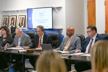 Members of the Alabama Educational Television Commission sit at a conference table during a meeting as a screen displays “Executive Director Highlights.”