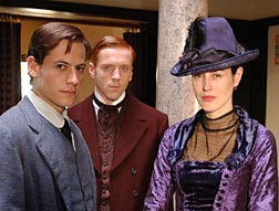 Two dudes and a chick looking like they want to get out of their starchy clothes. She is in purple satin with matching hat. Soames looks uneasy. Bosinney is more tousled.