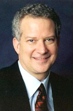 Lawson with curly graying hair, dark suit and dark red tie