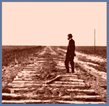 Photo of man in derby hat on newly laid ties for railroad