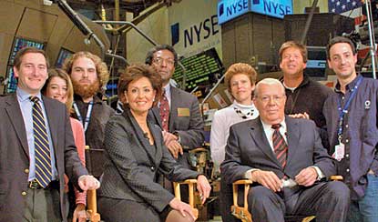 Nine "NBR" staffers pose on the NYSE floor, the anchors in folding chairs.