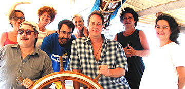 Eight staffers surround wheel of a sailing vessel