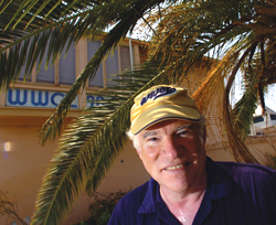 WWOZ's old studio building visible through palms, Freedman smiling in foreground